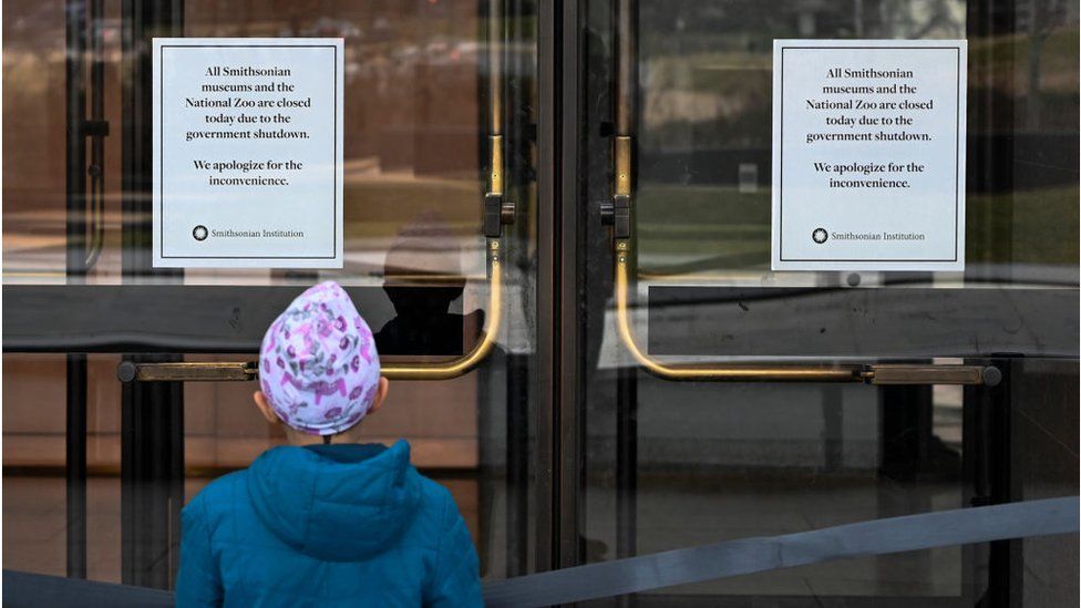 A young girl reads a sign posted on the door of The National Museum of African American History stating that all Smithsonian Museums are closed due to the partial shutdown of the US government