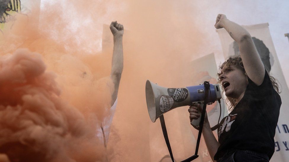 A protester with a megaphone stands in front of a cloud of smoke