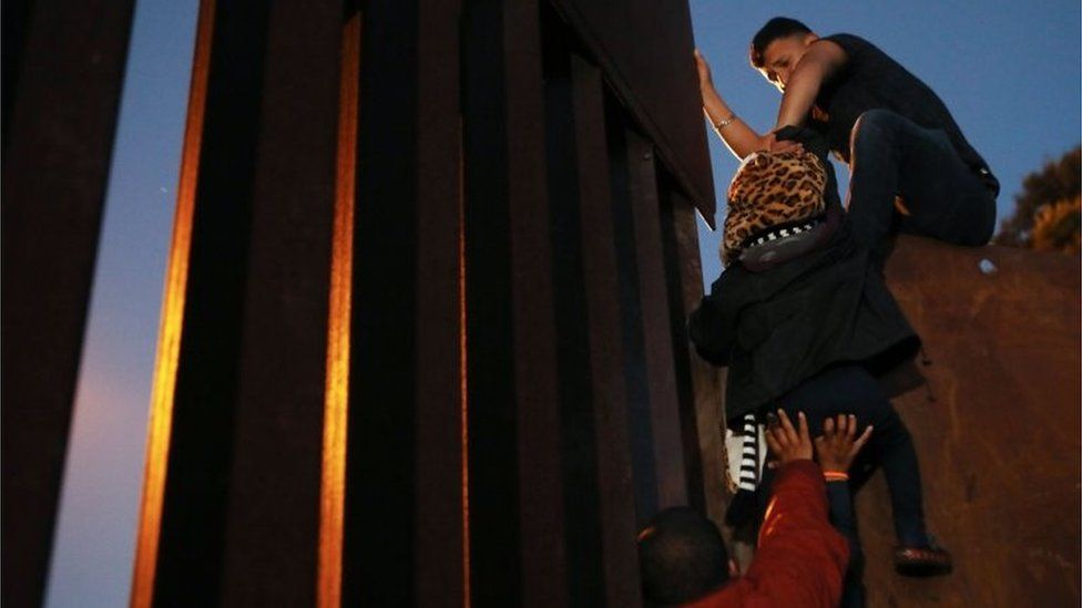 Members of the migrant caravan climb over the US-Mexico border fence on 3 December, 2018