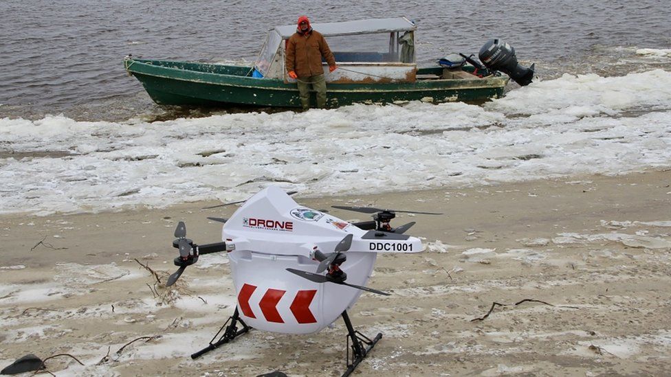 Drone sits on beach if front of a speed boat