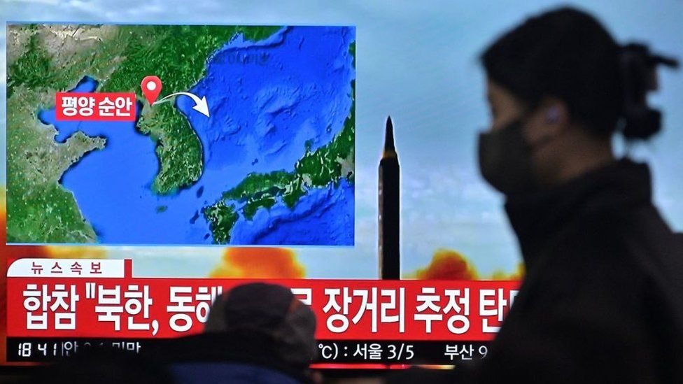 woman walks past a television showing a news broadcast with file footage of a North Korean missile test, at a railway station in Seoul on February 18, 2023. -