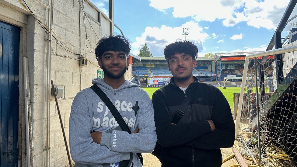 Umor Uddin (left) and Atif Khan (right) stood next to each other smiling with the Luton Town football ground in the background