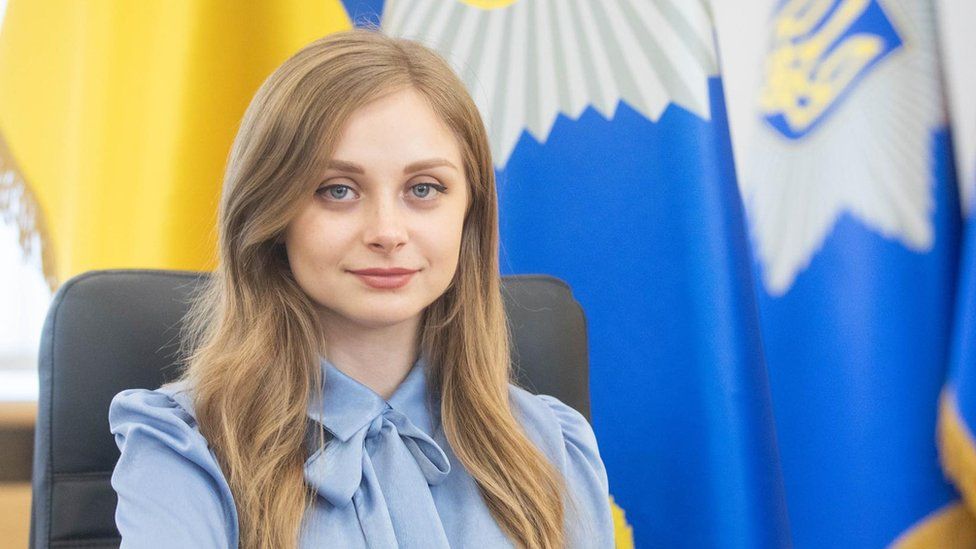 Tetiana Shutiak smiles for a photo in front of a Ukraine flag