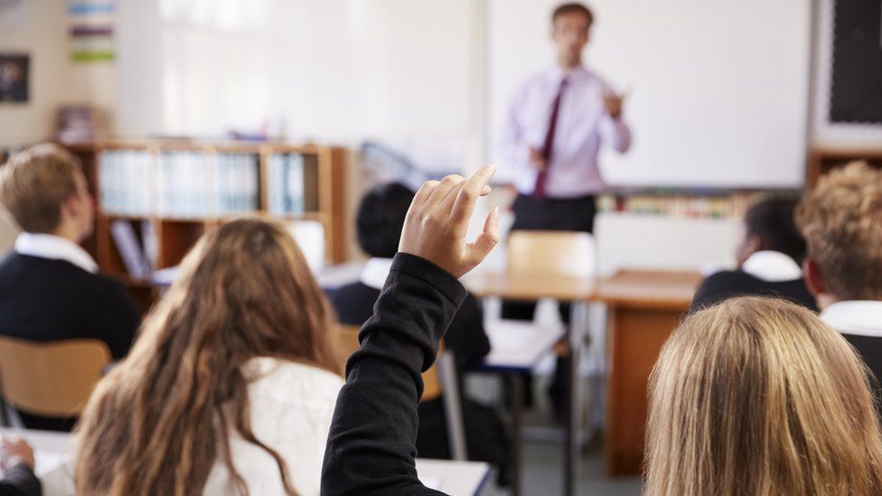 Female student raising her hand to ask a question in a classroom