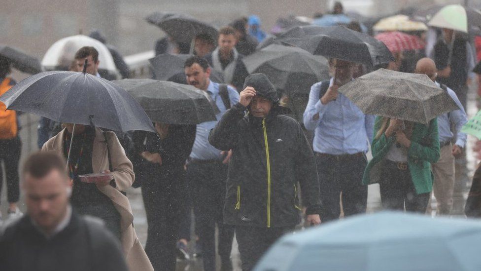 File image showing people with umbrellas and coats walking in the rain in London