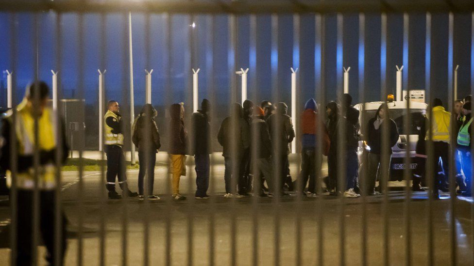 Security staff escort migrants after their incursion into the Eurotunnel site in Coquelles, northern France, on 3 October 2015