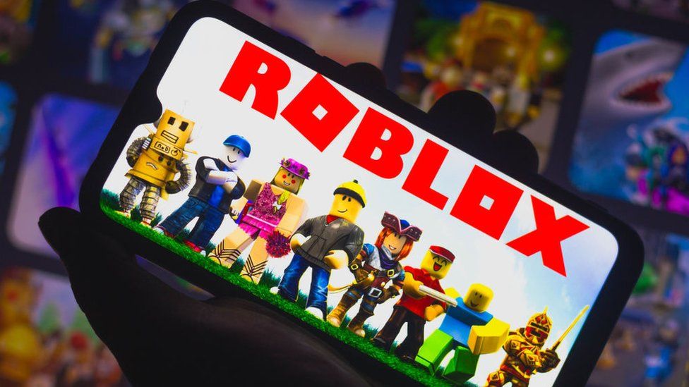 A hand holds up a phone with the Roblox logo on it