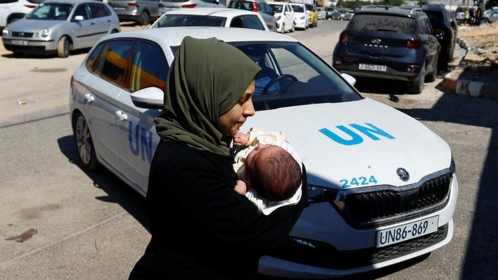 A woman carries her baby in front of a UN car at a United Nations center in Khan Younis in the southern Gaza Strip on 13 October 2023.