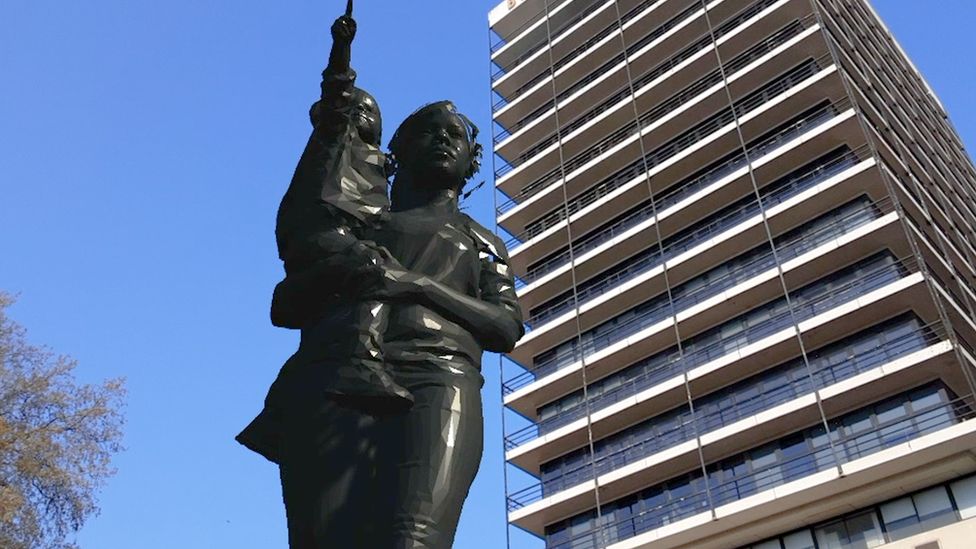 A virtual statue of a mother and child with the building formerly known as Colston Tower in the background