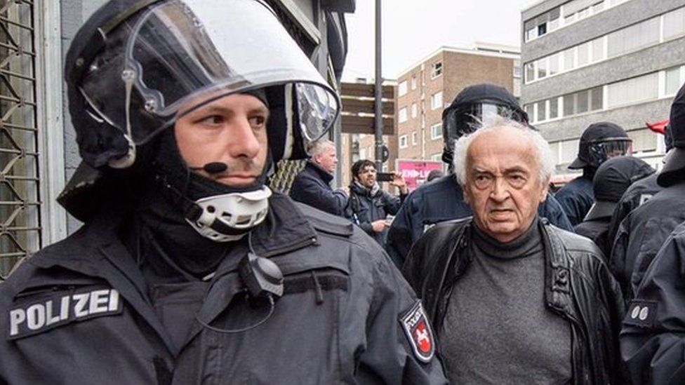 officers in riot gear flanking an elderly man