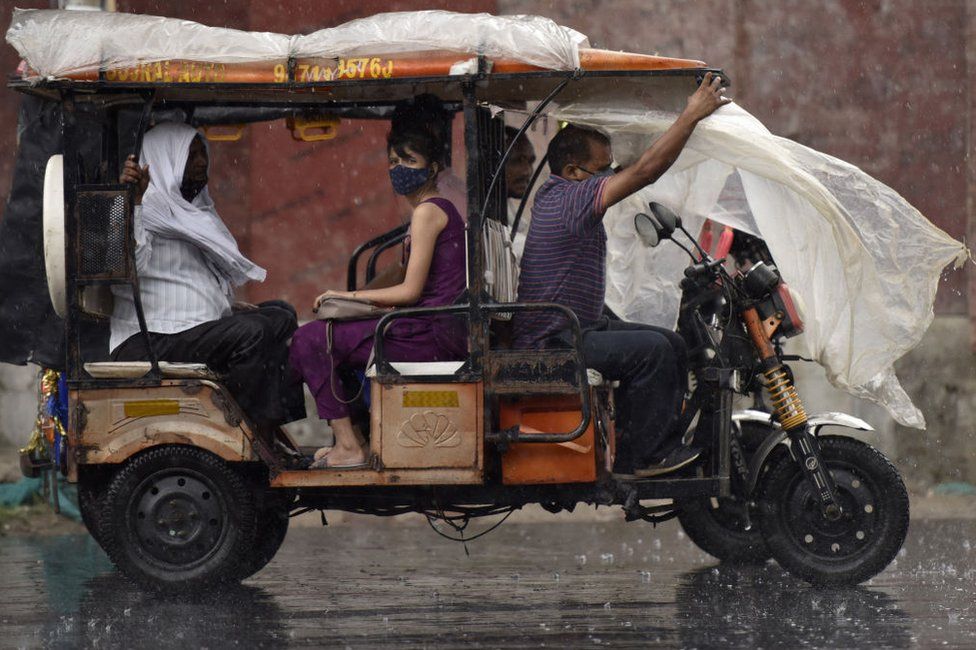 Commuters on an electric battery auto rickshaw as it rains, on September 24, 2021 in Noida, India.