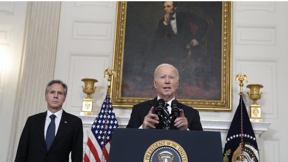Biden at podium in dark suit before portrait of Abraham Lincoln, Blinken to his right in dark suit and blue tie.