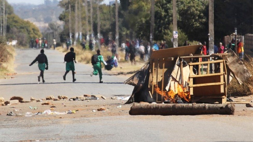 Schoolchildren run past a burning barricade, following a job boycott called via social media platforms, in Harare, Wednesday, July,6, 2016