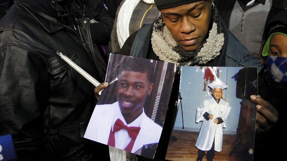 Janet Cooksey (L), birthmother of Quintonio LeGrier, walks away from an interview while a friend holds pictures of LeGrier shortly before a candlelight vigil in honour of Bettie Jones