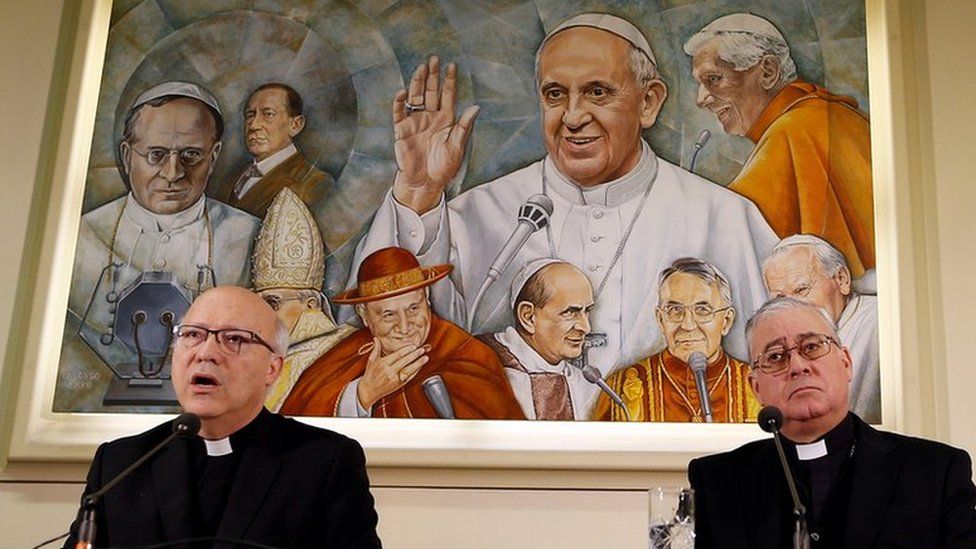 Chilean bishops Luis Fernando Ramos Perez and Juan Ignacio Gonzalez Errazuriz holding a news conference in front of a painting of the Pope