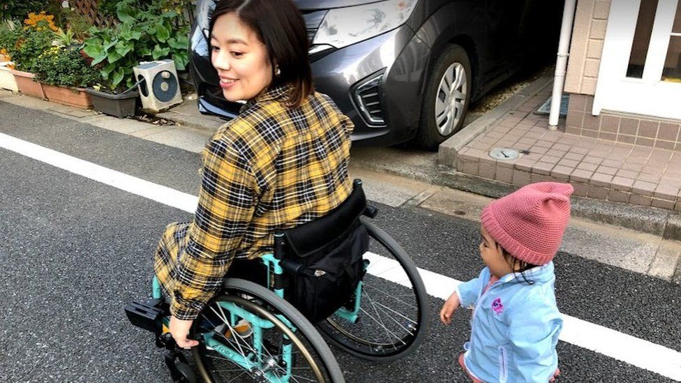 Mizuki in her wheelchair with one of her daughters following