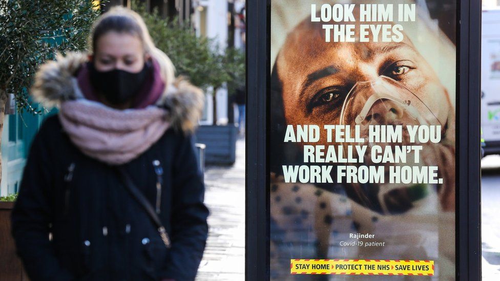 A woman wearing a face mask walks past a Covid-19 NHS campaign poster