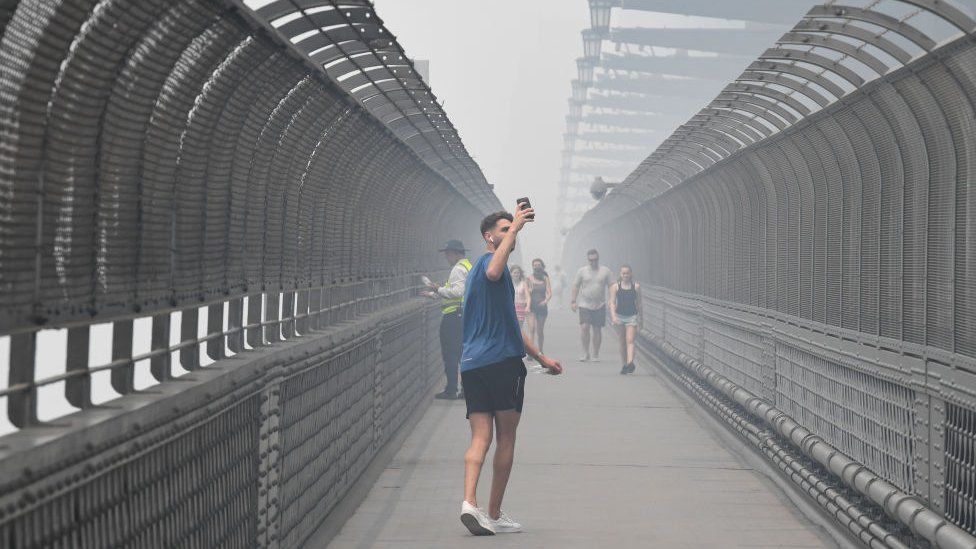 A man takes a photo as he crosses the Sydney Harbour Bridge amid heavy smoke