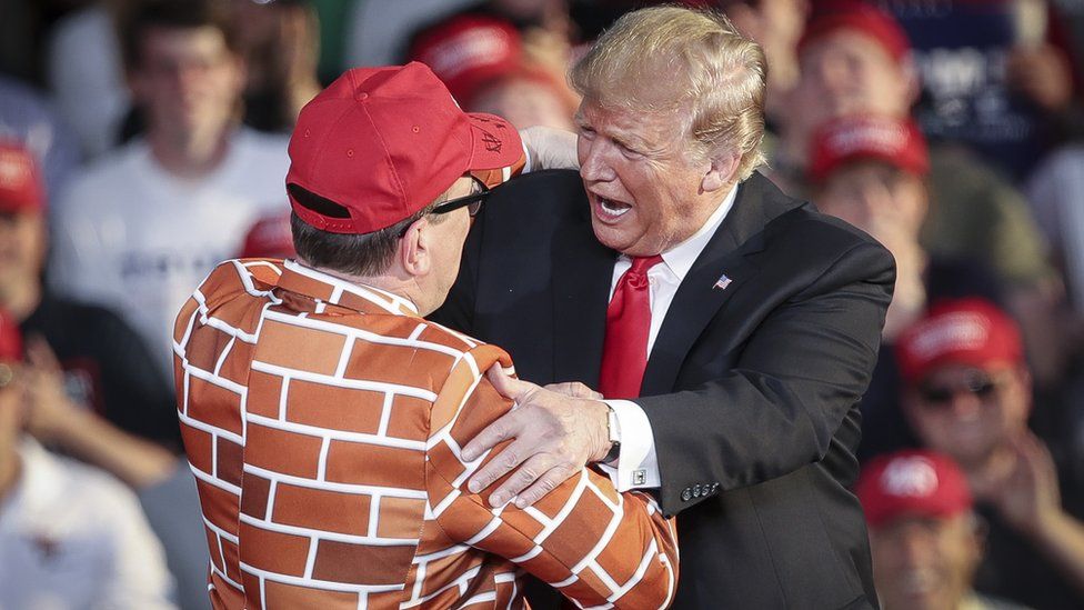 Trump greets a man dressed in a border wall suit during a rally