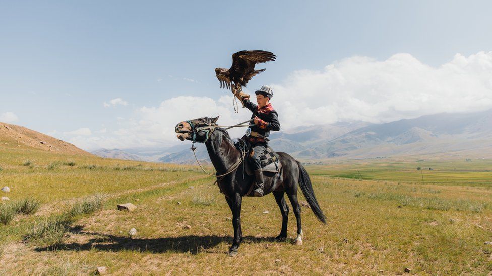 Hunter in traditional costume riding horse with Golden Eagle in Kyrgyzstan