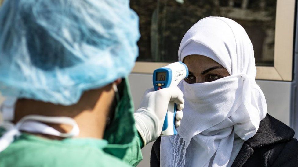 A medic checks the body temperature of a passenger, as a preventive measure against the coronavirus, upon her arrival by bus in Syria's Kurdish area