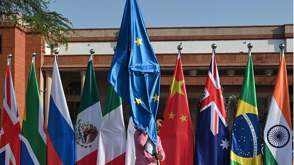 A worker carrying the flag of the European Union walks past the national flags of participating nations during the G20 foreign ministers' meeting in New Delhi on March 2, 2023.