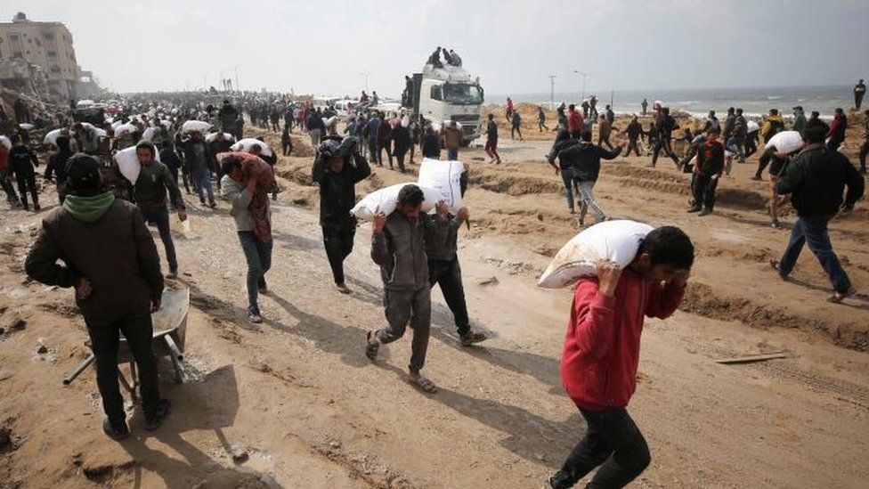 Palestinians carry bags of flour from an aid truck in Gaza City