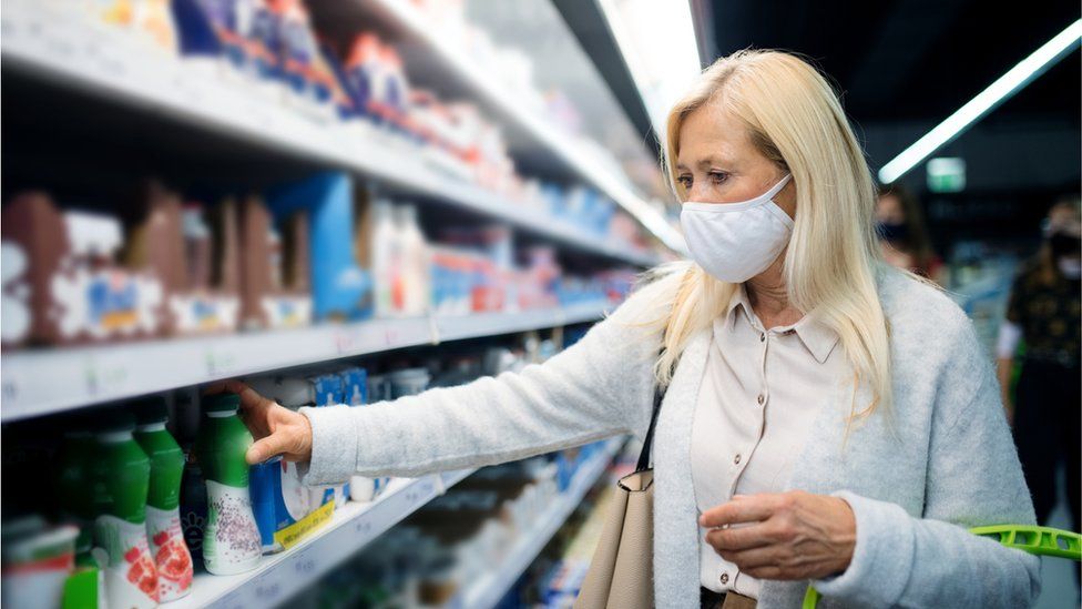 Стоковое изображение: Женщина с бакалеей лицевого щитка гермошлема покупая в супермаркете.