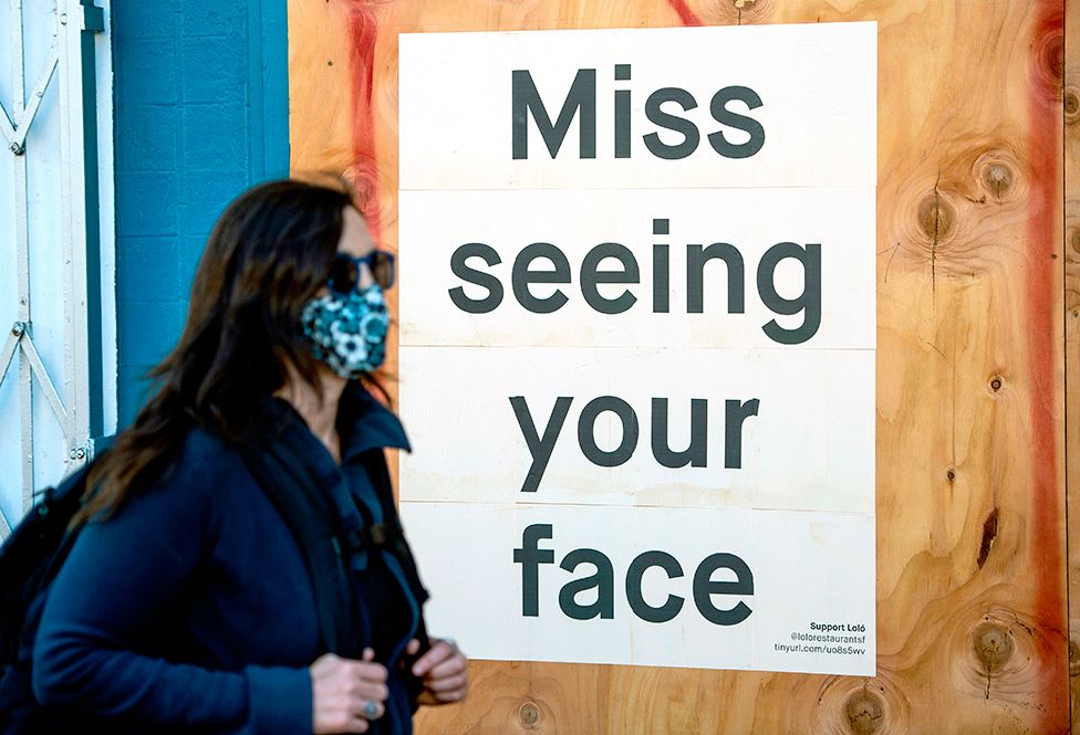 A woman in a face mask walks past a sign