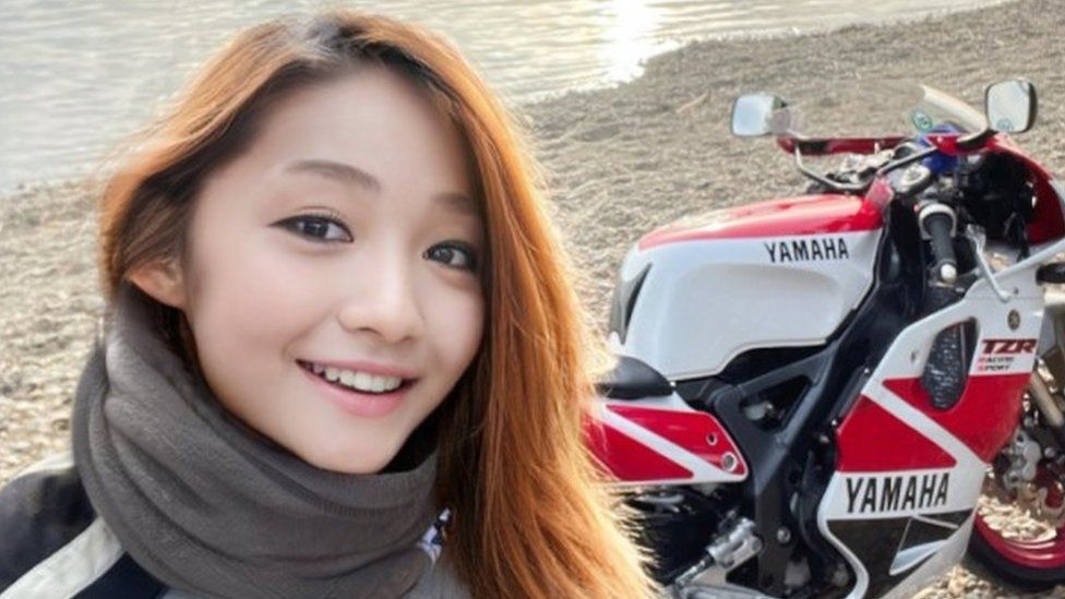  Japanese biker claiming to be a woman posing in front of motor cycle. 