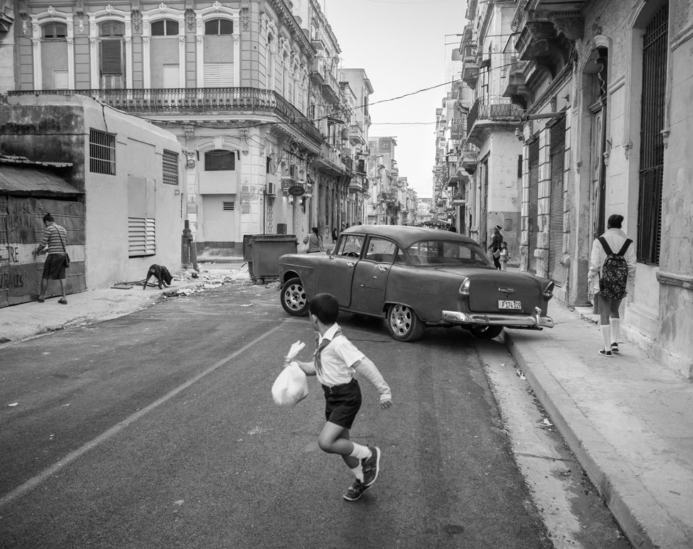 Черно-белая фотография ребенка, смотрящего на машину, бегущую по улице