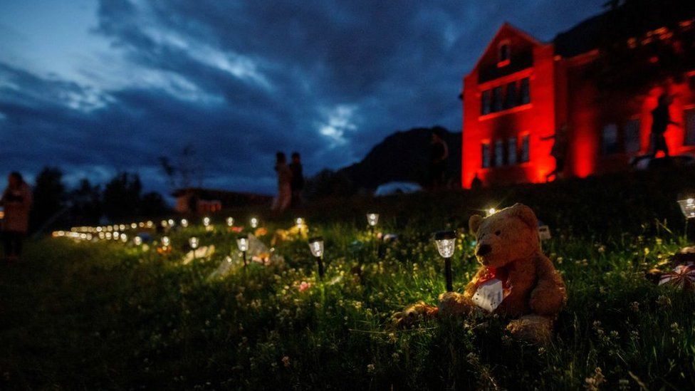 A teddy bear sits beside a lantern and momentous outside the former Kamloops Indian Residential School where flowers and cards have been left as part of a growing makeshift memorial to honour the 215 children whose remains have been discovered buried near the facility in Kamloops on June 5, 2021.
