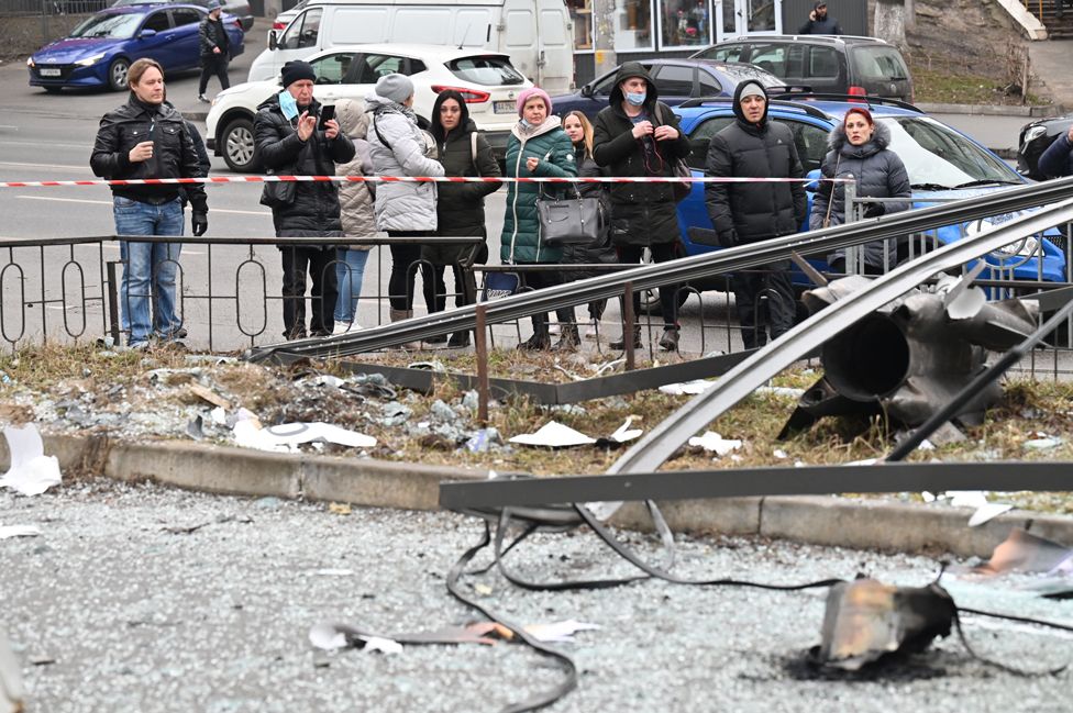People react standing behind the cordoned off area around the remains of a shell in Kyiv on 24 February 2022
