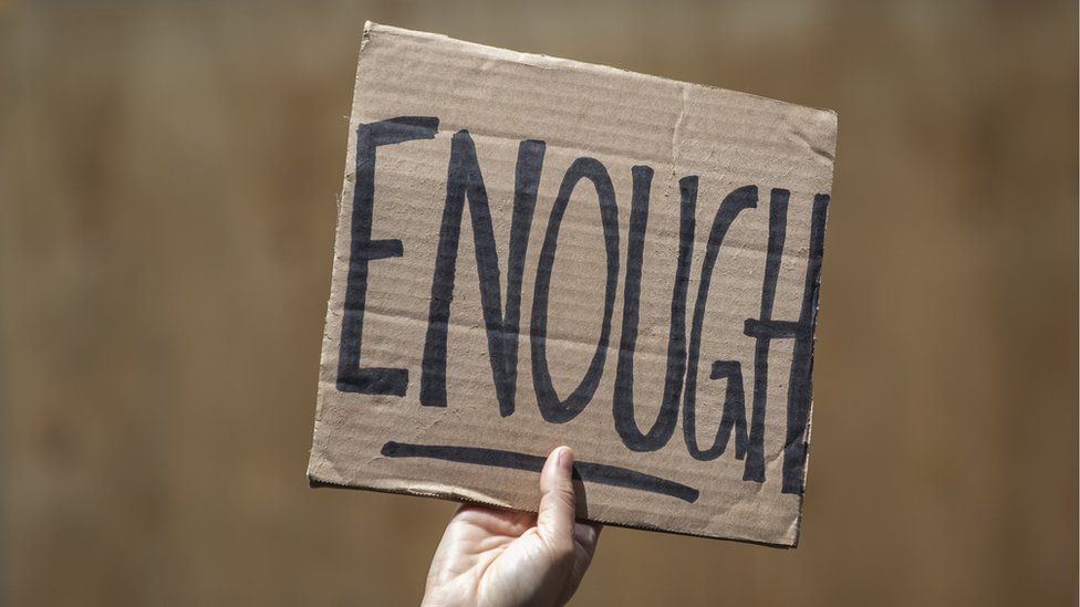 A person holds up a sign that reads 'Enough'