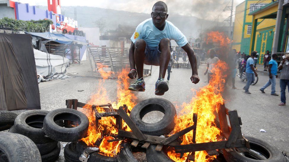 A protester jumps over a burning barricade during a protest against the government in the streets of Port-au-Prince