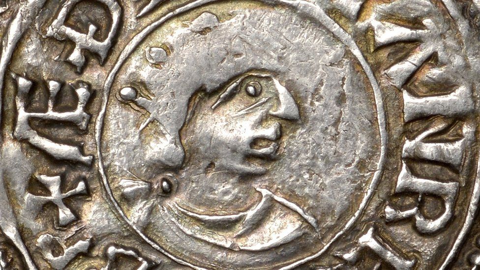 An old, worn silver penny with the outline of a King facing right wearing a crown and an old inscription round the edge.