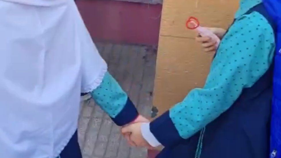 Two girls holding hands outside their school in Tehran after it was attacked