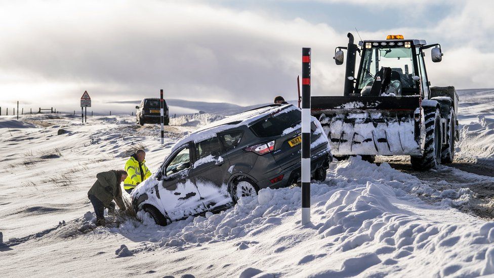 Car being dug out of snow with the help of a tractor during Storm Arwen