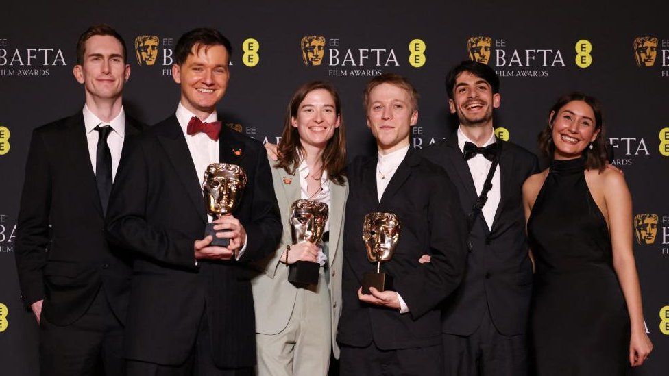 Line of people in formal clothing in front of a Bafta backdrop