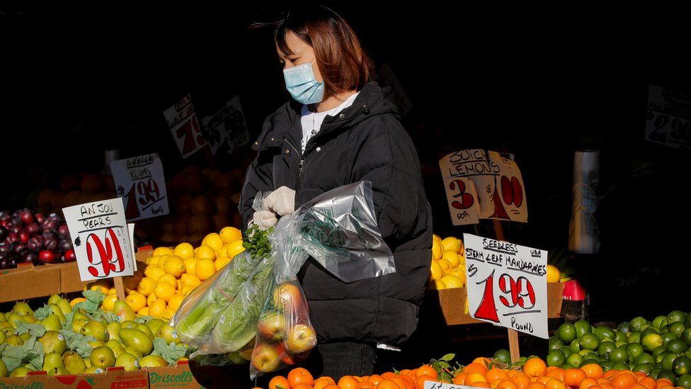 A woman wears a mask and gloves as he shops at a fruit stand in New York