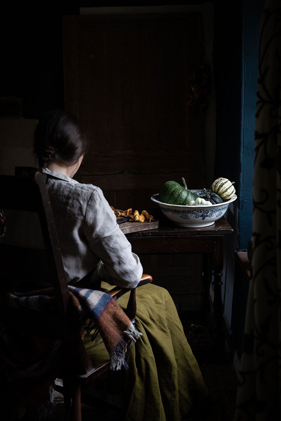 A woman sits at a table with a bowl of squash in front of her