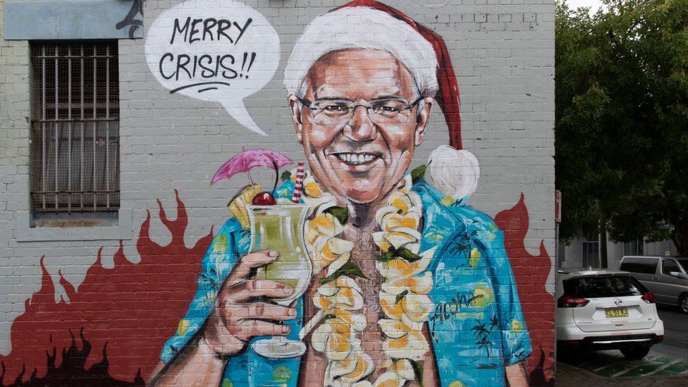 A wall mural depicting Scott Morrison, dressed in a Hawaiian shirt and Santa hat while holding a cocktail against a backdrop of flames, saying "Merry Crisis".