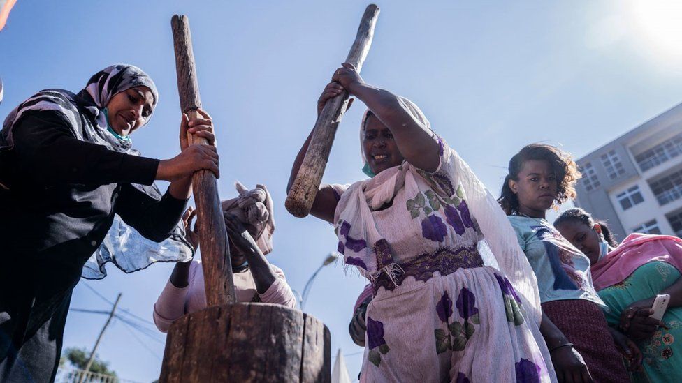 Women with large pounders pounding traditional food. One woman has the pounder raised high in the air and has an exhausted expression on her face in Addis Ababa, Ethiopia - Friday 19 November 2021