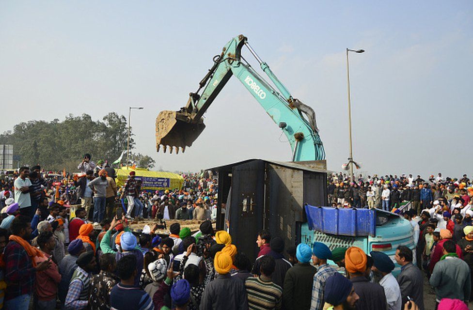 Farmers gather around a modified excavator brought to clear the police blockade of a highway stopping farmers from marching to New Delhi during an ongoing protest demanding minimum crop prices