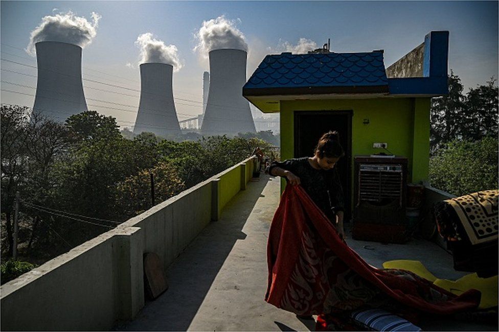 In this photograph taken on April 6, 2022, a girl folds a blanket at her house rooftop near the Thermal Power Corporation (NTPC) plant in Dadri.