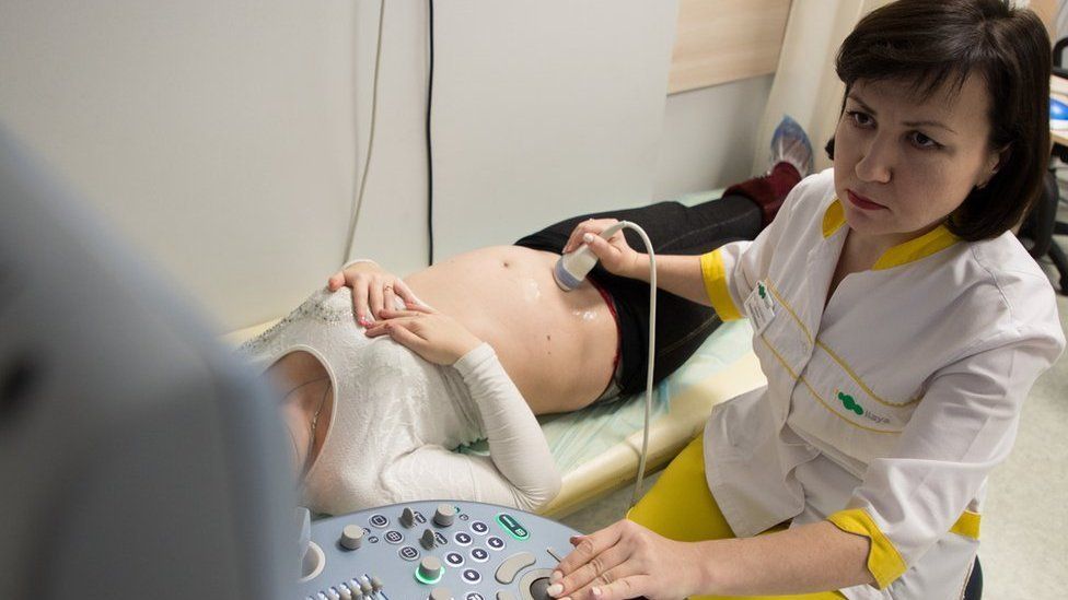 A doctor runs an ultrasound probe over the stomach of a pregnant surrogate at the Ilaya clinic