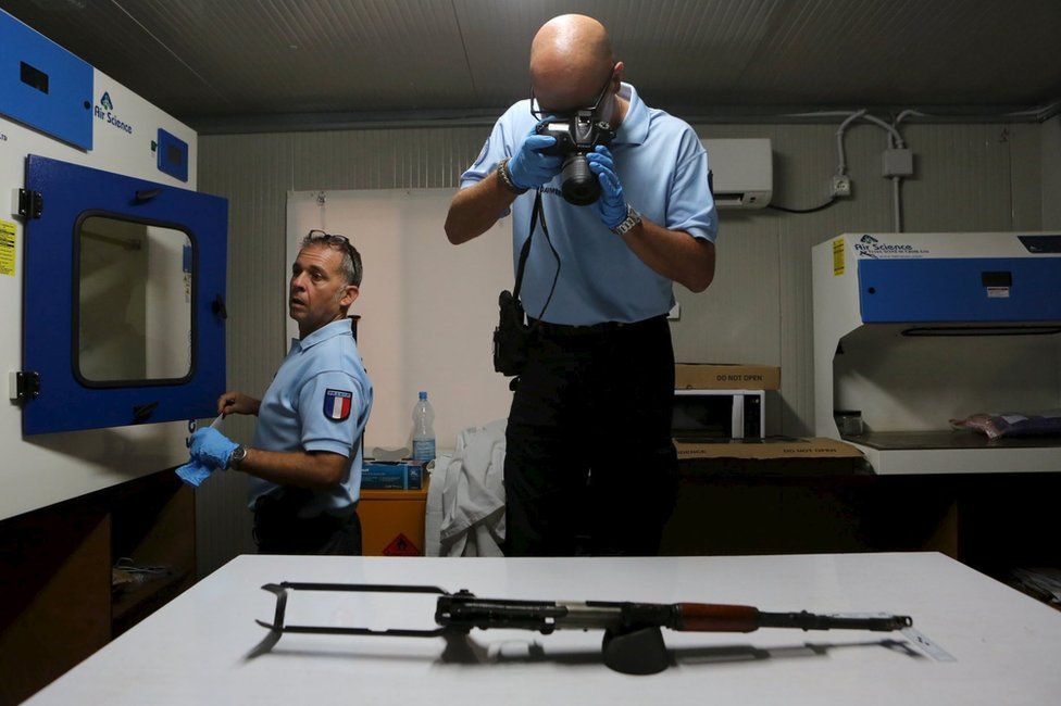 A French gendarme working for the UN photographs an AK-47 used by gunmen in the Radisson Blu hotel attack on a table in a lab in Bamako, Mali