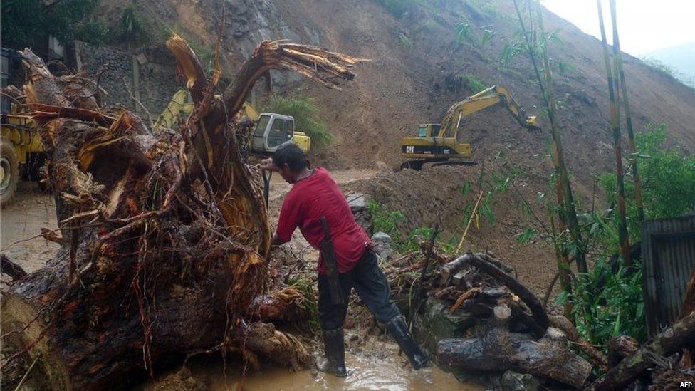 Worker cuts up fallen tree as heavy equipment clears debris and soil after a landslip due to heavy rains on a main road into Baguio City 22/08/2015