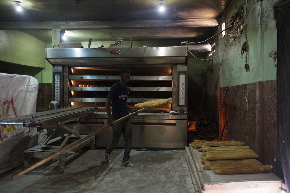 Kalilou Sow takes freshly baked bread out of the oven at Guemou Coura Bakery in Bamako, Mali on 2 February 2019