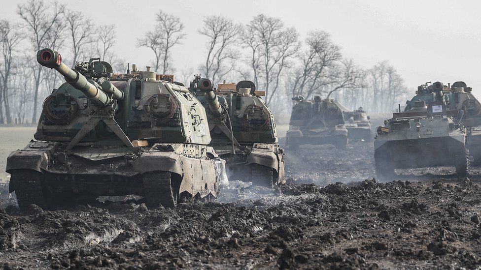 A tank and other armoured vehicles sit on a mud road